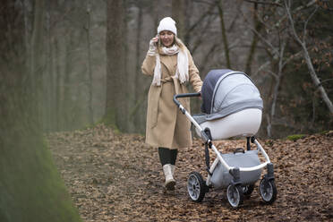 Woman with baby stroller talking on smart phone in forest - NJAF00275
