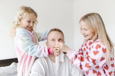Glückliche Töchter putzen die Nase des Vaters mit einer Serviette zu Hause ab - SIF00675