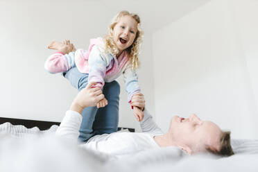 Happy daughter having fun and playing with father on bed at home - SIF00677