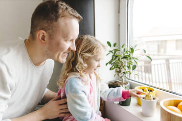 Ein glücklicher Vater und seine Tochter kümmern sich um die Pflanzen auf der Fensterbank zu Hause - SIF00687