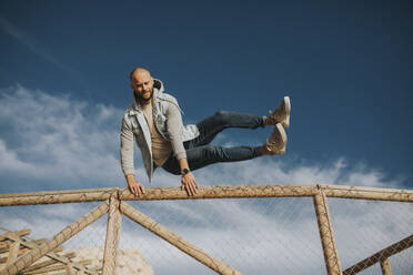 Man jumping over fence under sky - DMGF01043