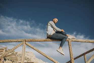 Man sitting on fence under sky - DMGF01044