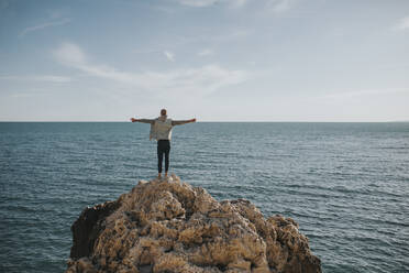Man standing with arms stretched on rock in front of sea - DMGF01047