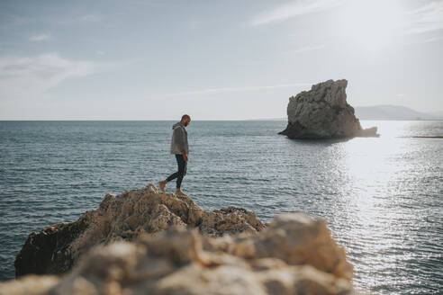 Mann geht auf Felsen vor dem Meer - DMGF01049
