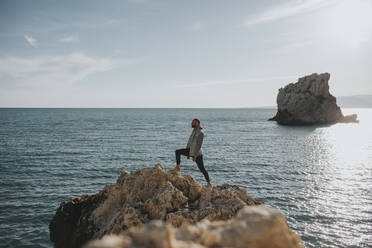 Man standing on rock in front of sea at sunset - DMGF01050