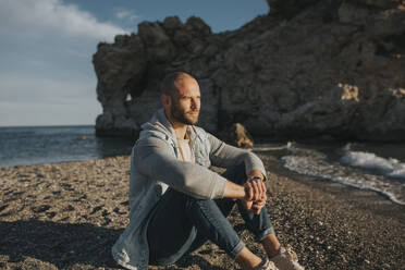 Nachdenklicher Mann sitzt bei Sonnenuntergang am Strand - DMGF01054