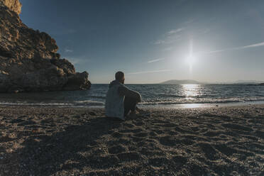 Nachdenklicher Mann sitzt bei Sonnenuntergang am Strand - DMGF01055