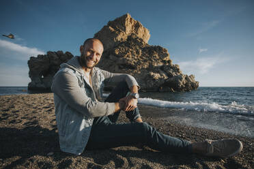 Glücklicher Mann sitzt bei Sonnenuntergang am Strand - DMGF01056