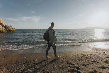 Mann mit Rucksack geht am Strand spazieren - DMGF01057