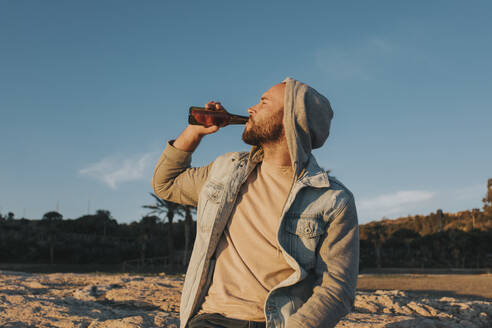 Man drinking beer at sunset under sky - DMGF01062