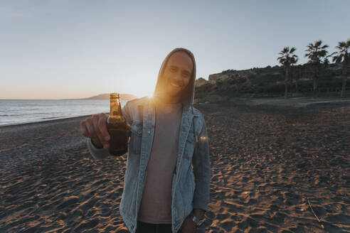 Smiling man standing with beer bottle at sunset - DMGF01069