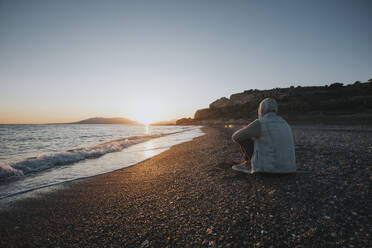 Man sitting on shore at sunset beach - DMGF01072