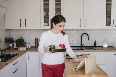 Woman with vegetable using tablet PC in kitchen at home - EBBF08127