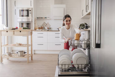 Woman arranging crockery in dishwasher at home - EBBF08140