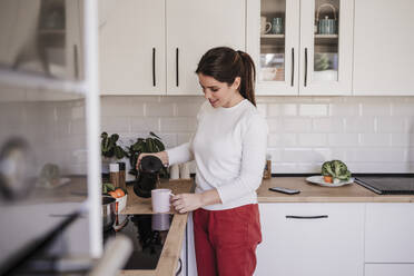 Woman pouring coffee in cup at kitchen - EBBF08145