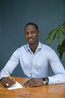 Businessman with paper and pencil sitting at desk - AXHF00370