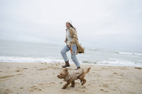 Frau läuft mit Hund in der Nähe des Ufers am Strand - ALKF00161