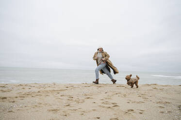 Frau läuft mit Hund auf Sand am Strand - ALKF00162