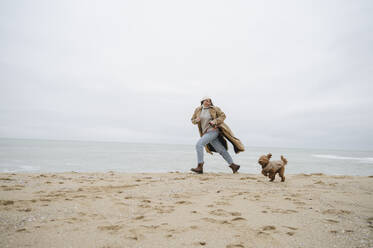 Woman running with dog on sand at beach - ALKF00162