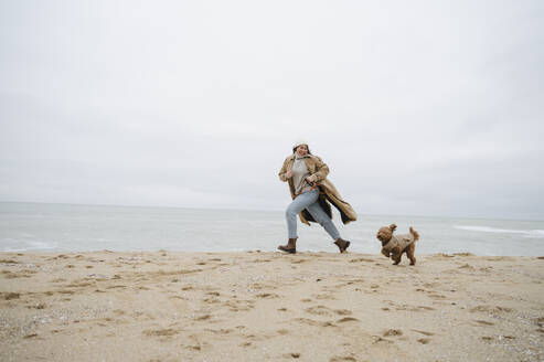 Frau läuft mit Hund auf Sand am Strand - ALKF00162