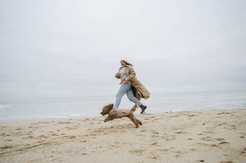 Junge Frau spielt mit Hund im Sand am Strand - ALKF00163