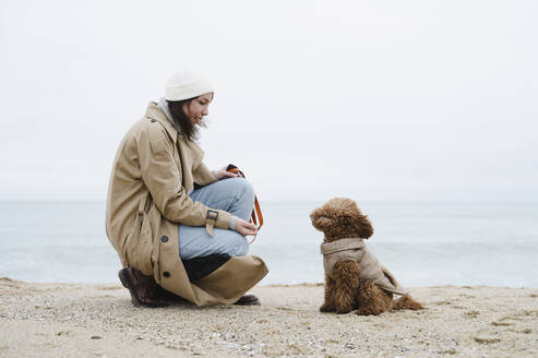 Junge Frau hockt bei einem Hund am Strand - ALKF00165