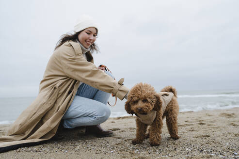 Lächelnde Frau streichelt Hund am Strand - ALKF00166
