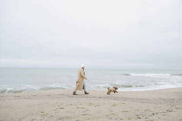 Woman strolling with dog near shore at beach - ALKF00168