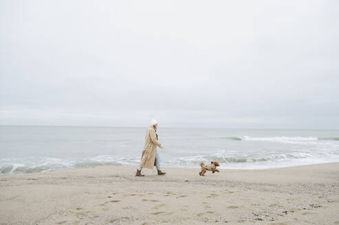 Frau spaziert mit Hund in der Nähe des Ufers am Strand - ALKF00168