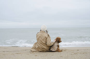 Frau schaut auf das Meer und sitzt mit Hund am Ufer - ALKF00170