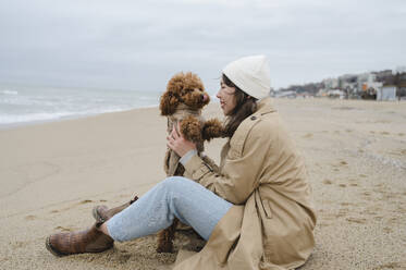 Woman enjoying with pet dog sitting at beach - ALKF00172