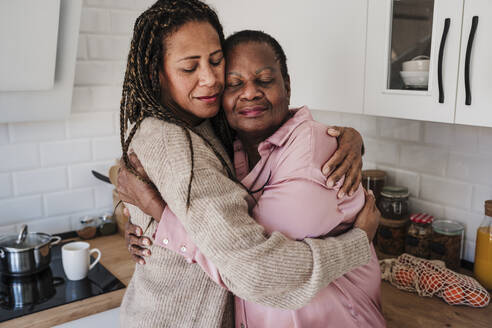 Woman with eyes closed embracing mother in kitchen at home - EBBF08187