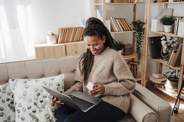 Glückliche Frau beim Online-Shopping mit Laptop und Kreditkarte zu Hause - EBBF08214