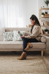 Woman using laptop sitting on sofa at home - EBBF08217