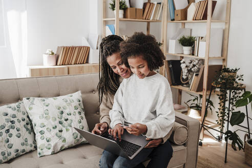 Tochter beim Online-Shopping mit der Mutter über den Laptop auf dem Sofa zu Hause - EBBF08221