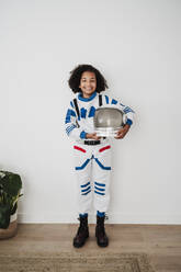 Elementary girl wearing space suit standing in front of white wall - EBBF08234