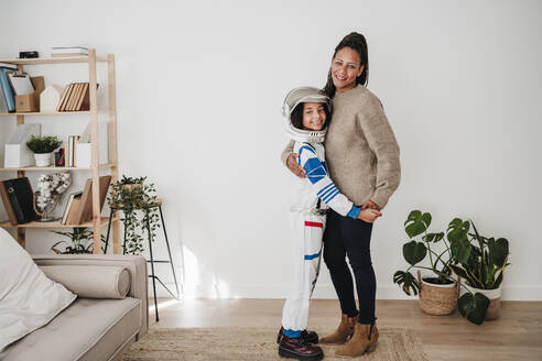 Girl wearing space suit embracing mother near wall at home - EBBF08262