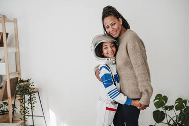 Smiling girl wearing space suit embracing mother at home - EBBF08264