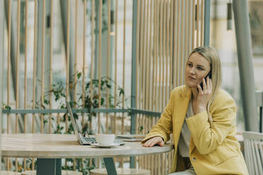 Geschäftsfrau, die in einem Café sitzt und mit ihrem Handy spricht - VSNF00596