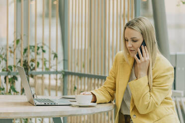 Blond businesswoman talking on smart phone sitting at cafe - VSNF00597