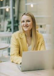 Lächelnde Geschäftsfrau mit Laptop in einem Café sitzend - VSNF00598