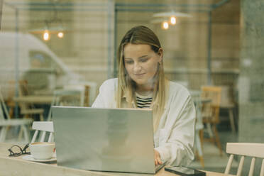 Blond businesswoman using laptop sitting at cafe - VSNF00609