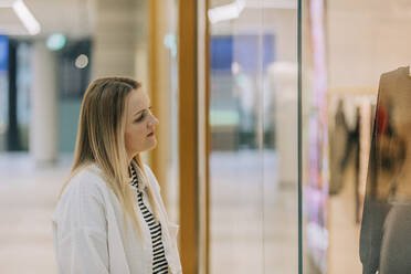 Frau schaut durch ein Schaufenster auf eine Schaufensterpuppe in einem Einkaufszentrum - VSNF00612