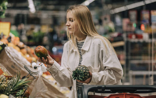 Woman with blond hair examining fruits in supermarket - VSNF00620