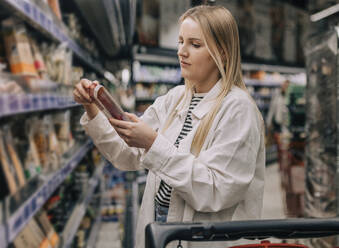 Frau betrachtet Lebensmittelverpackung im Supermarkt - VSNF00621