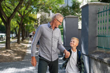 A happy grandfather taking his grandson home from school, walking outdoors in street. - HPIF08321