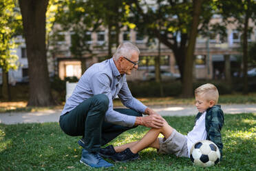 Ein kleiner Junge mit einem verletzten Bein erhält von seinem Großvater im Park einen Gips. - HPIF08326