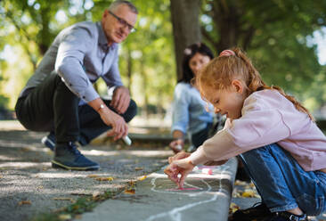 Ein älteres Ehepaar mit Enkelkindern zeichnet mit Kreide auf dem Bürgersteig im Park. - HPIF08327