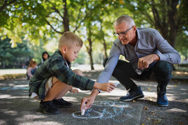 Ein Großvater mit Enkel zeichnet mit Kreiden auf dem Bürgersteig im Park. - HPIF08328
