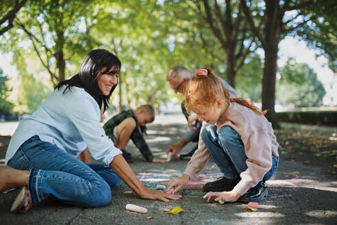 Ein älteres Ehepaar mit Enkelkindern zeichnet mit Kreide auf dem Bürgersteig im Park. - HPIF08331